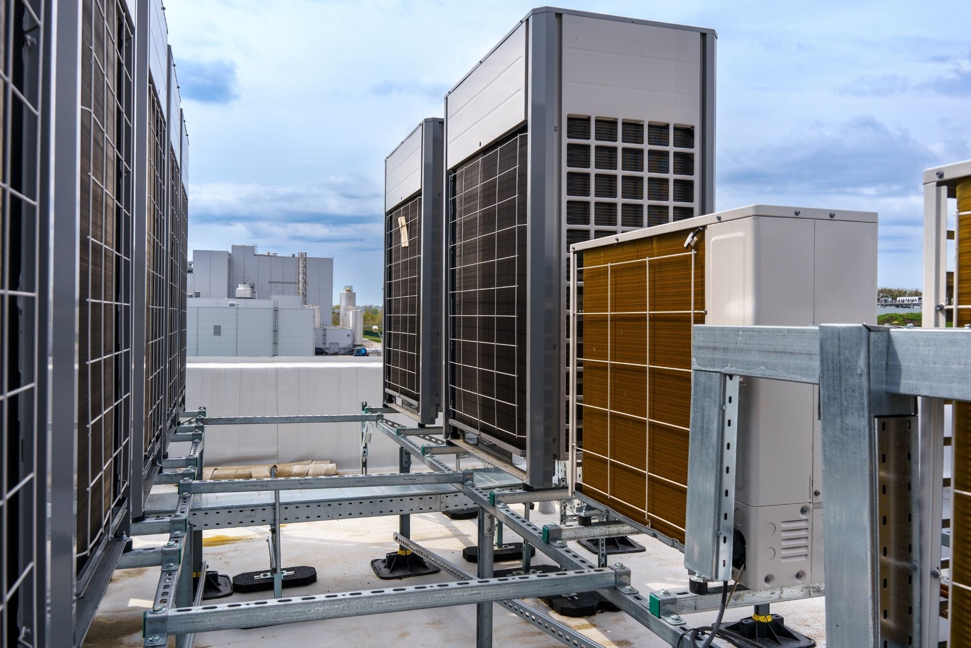 HVAC technician wearing mask and hard hat, working on AC units on a rooftop.
