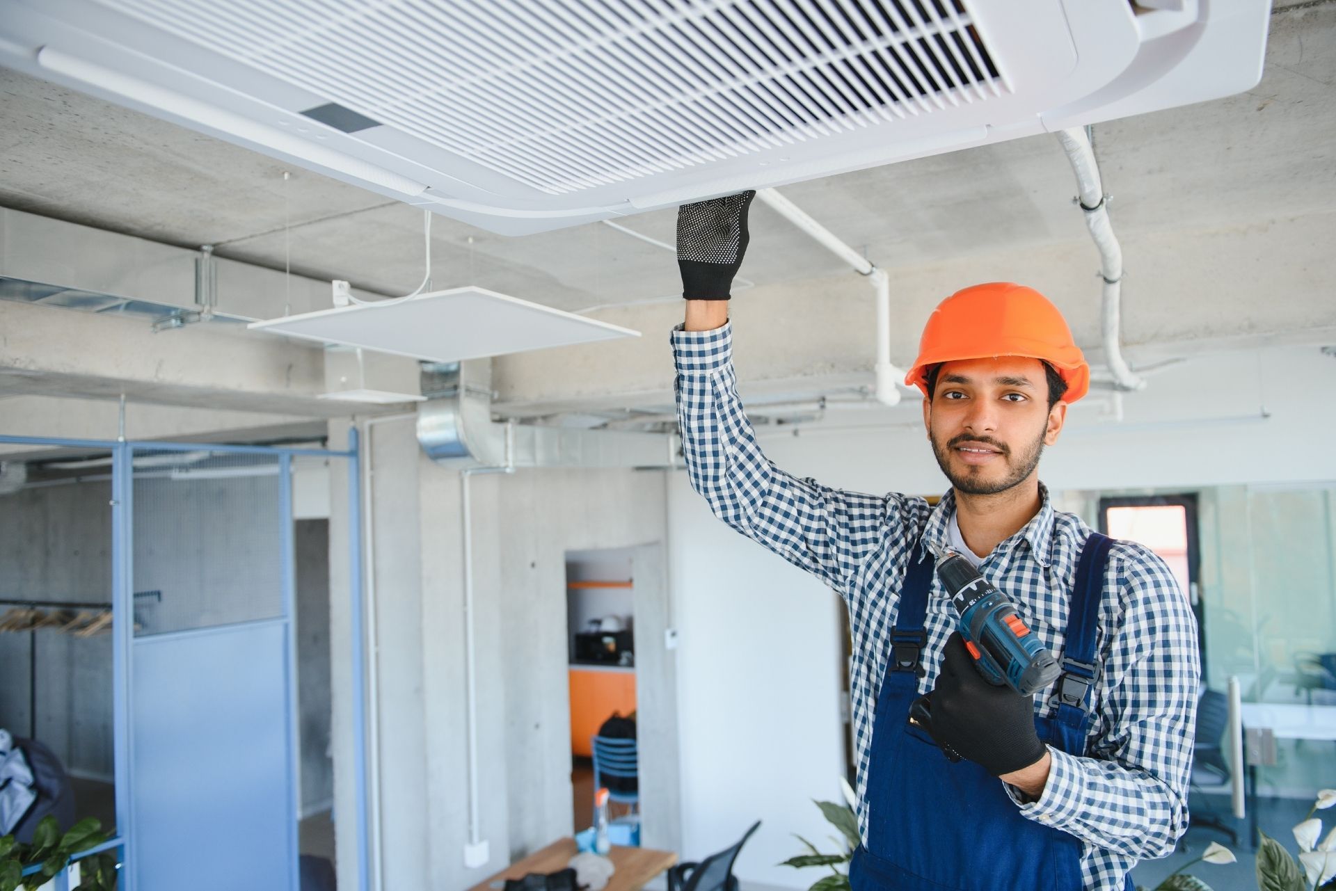 HVAC technician wearing mask and hard hat, working on AC units on a rooftop. HVAC technician wearing mask and hard hat, working on AC units on a rooftop.