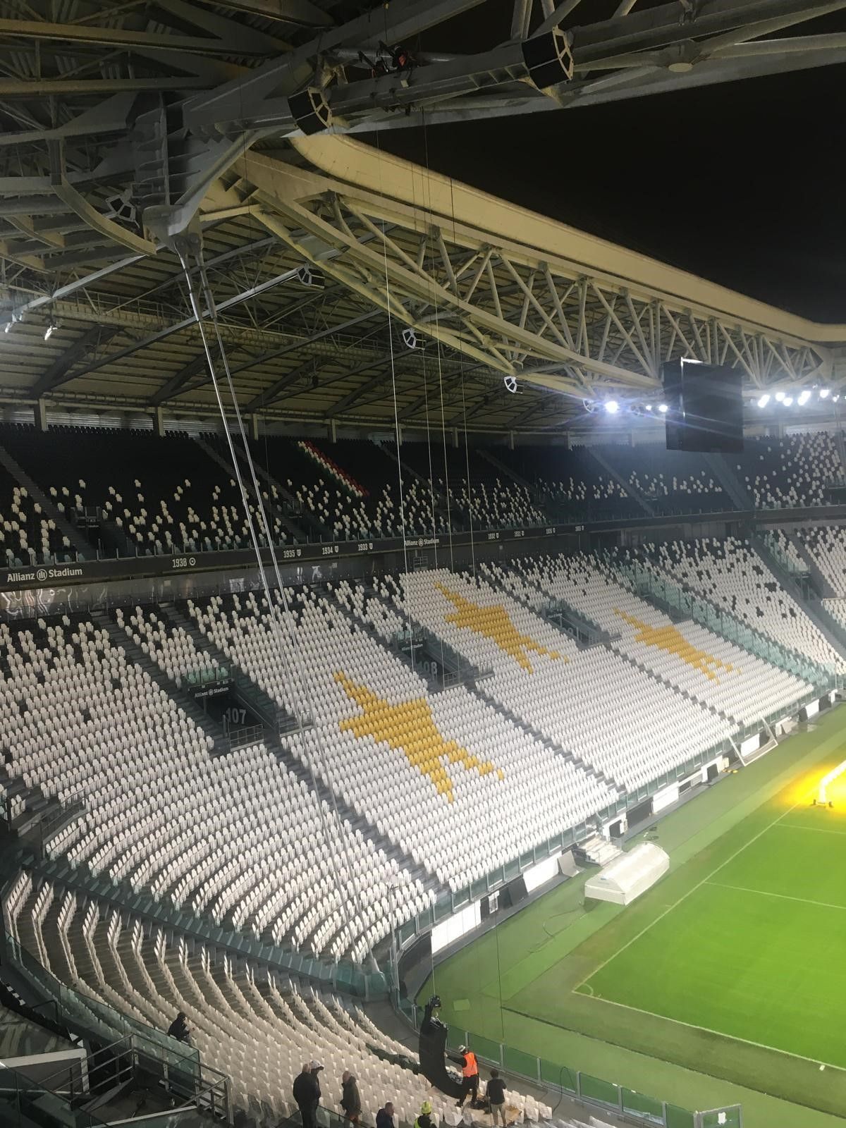 Sedili vuoti dello stadio, alcuni con motivi a stella, sotto luci intense.