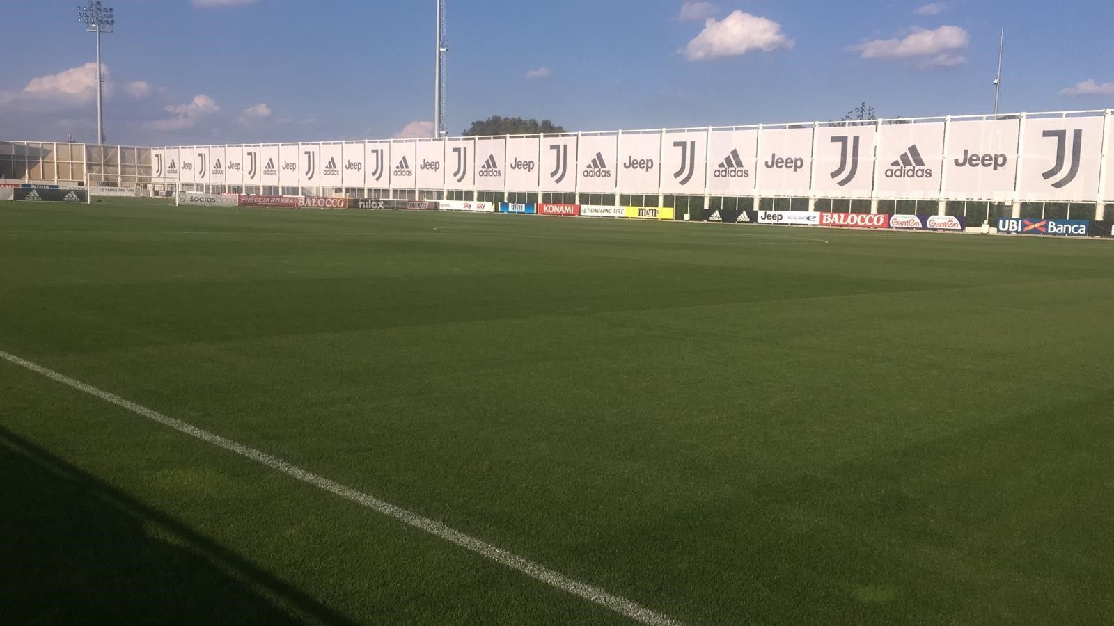 Campo da calcio verde con i loghi della Juventus su un lungo striscione sotto un cielo azzurro.