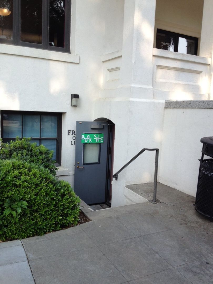 A white building with a green book sale sign on the door