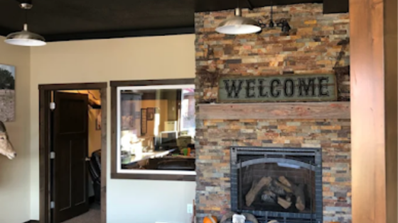 Lobby with a brick fireplace and a “WELCOME” sign, viewed through a windowed interior wall.