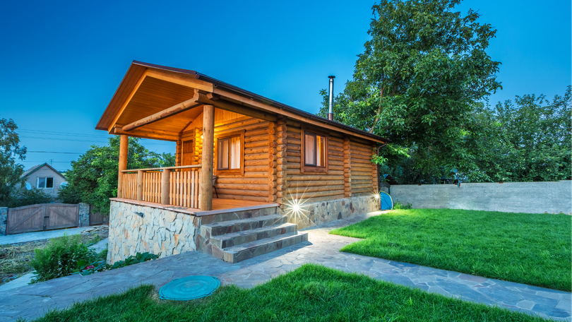 Wooden cabin with stone steps and a green lawn at dusk