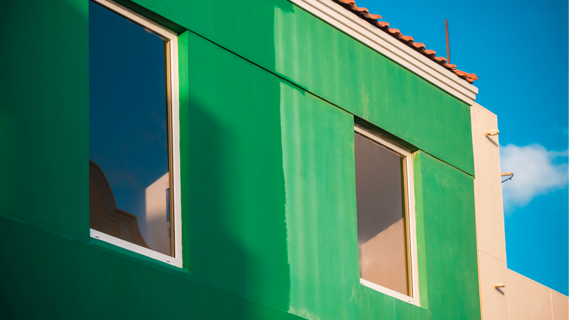 Green building facade with two windows against a blue sky