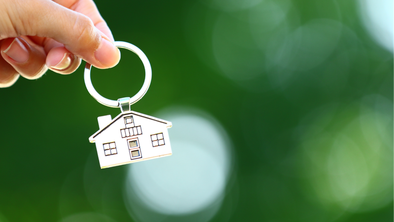 Hand holding a house-shaped keychain against a blurred green background