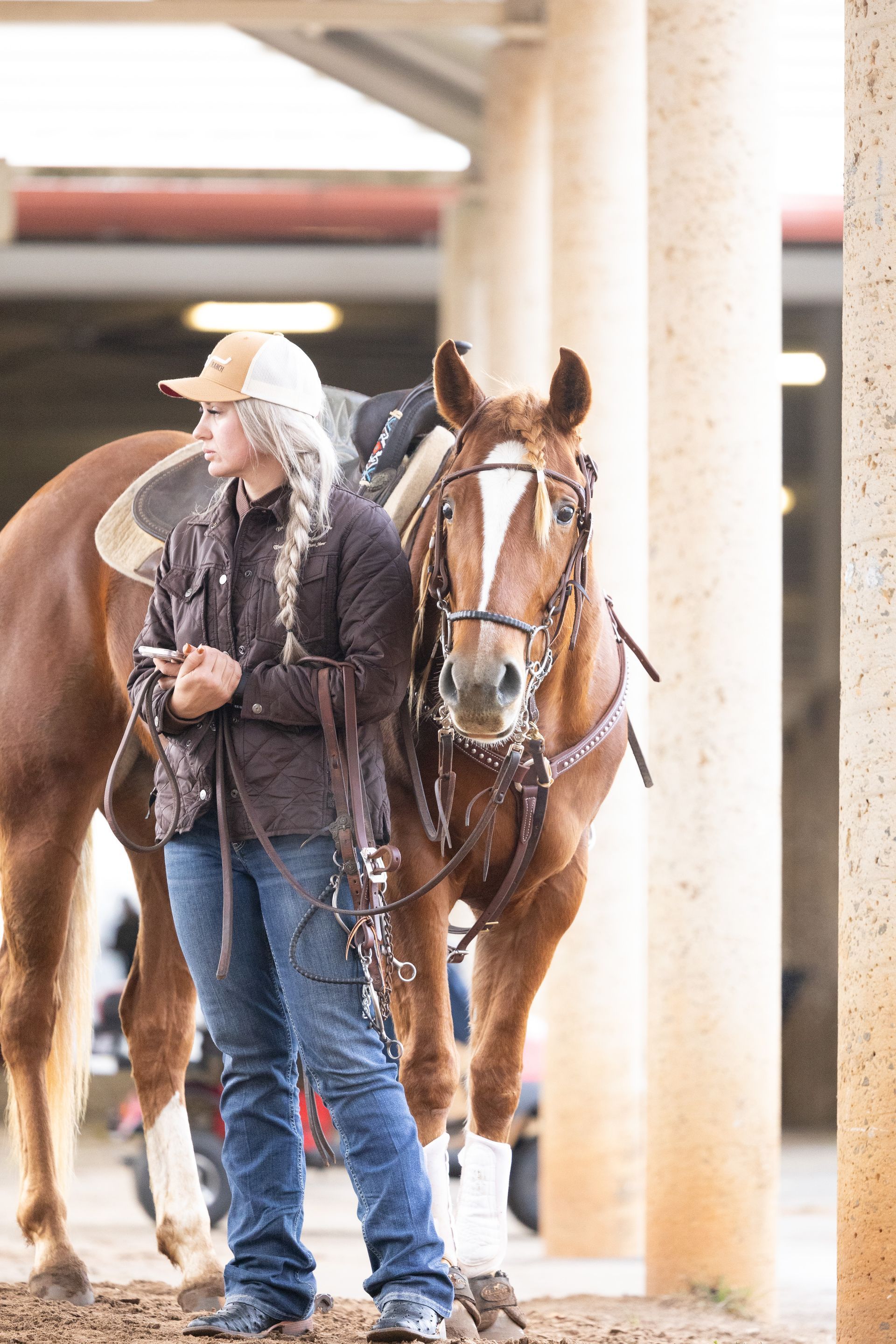 A woman is standing next to a brown horse in a stable.