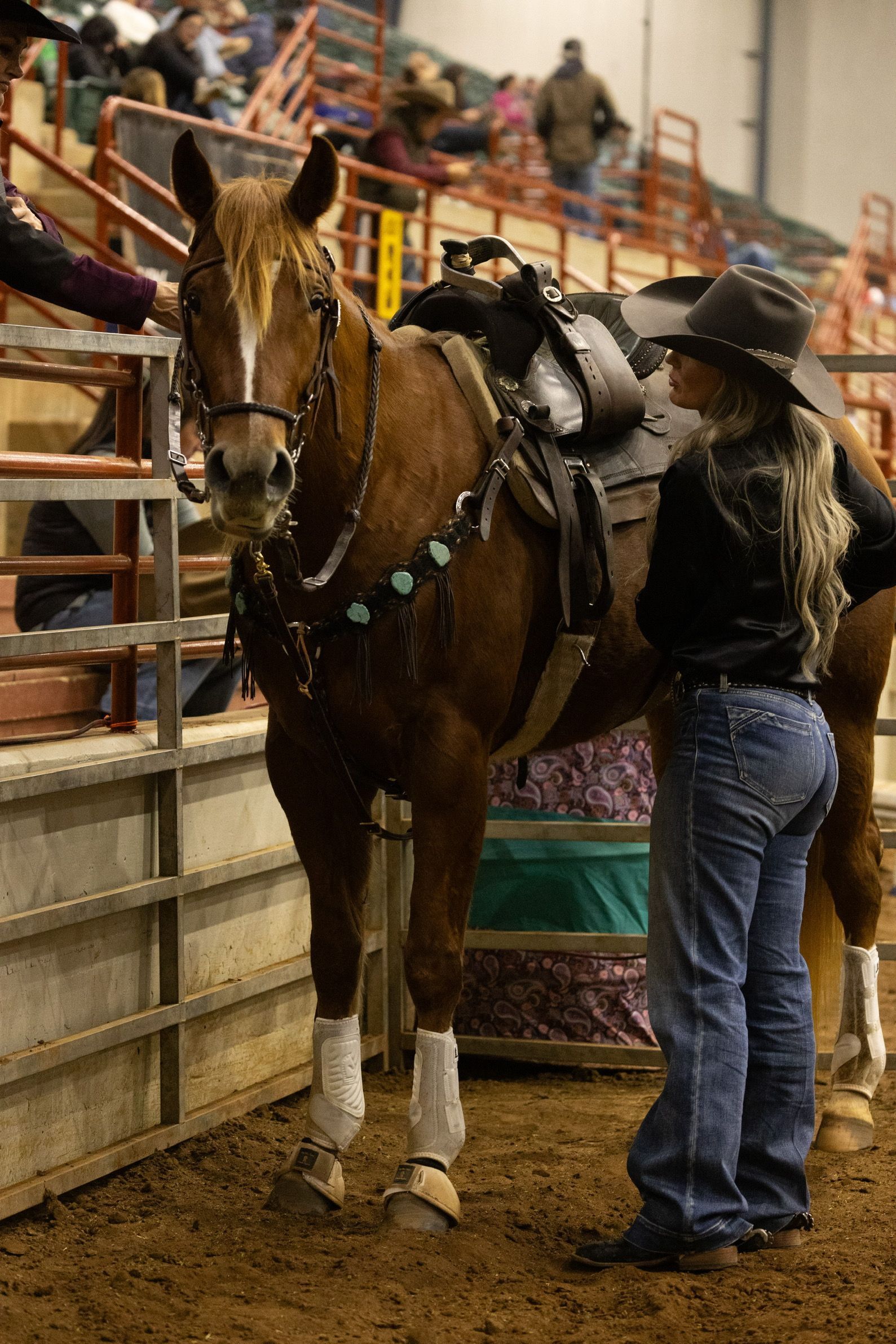 A woman is standing next to a brown horse with a saddle on it.