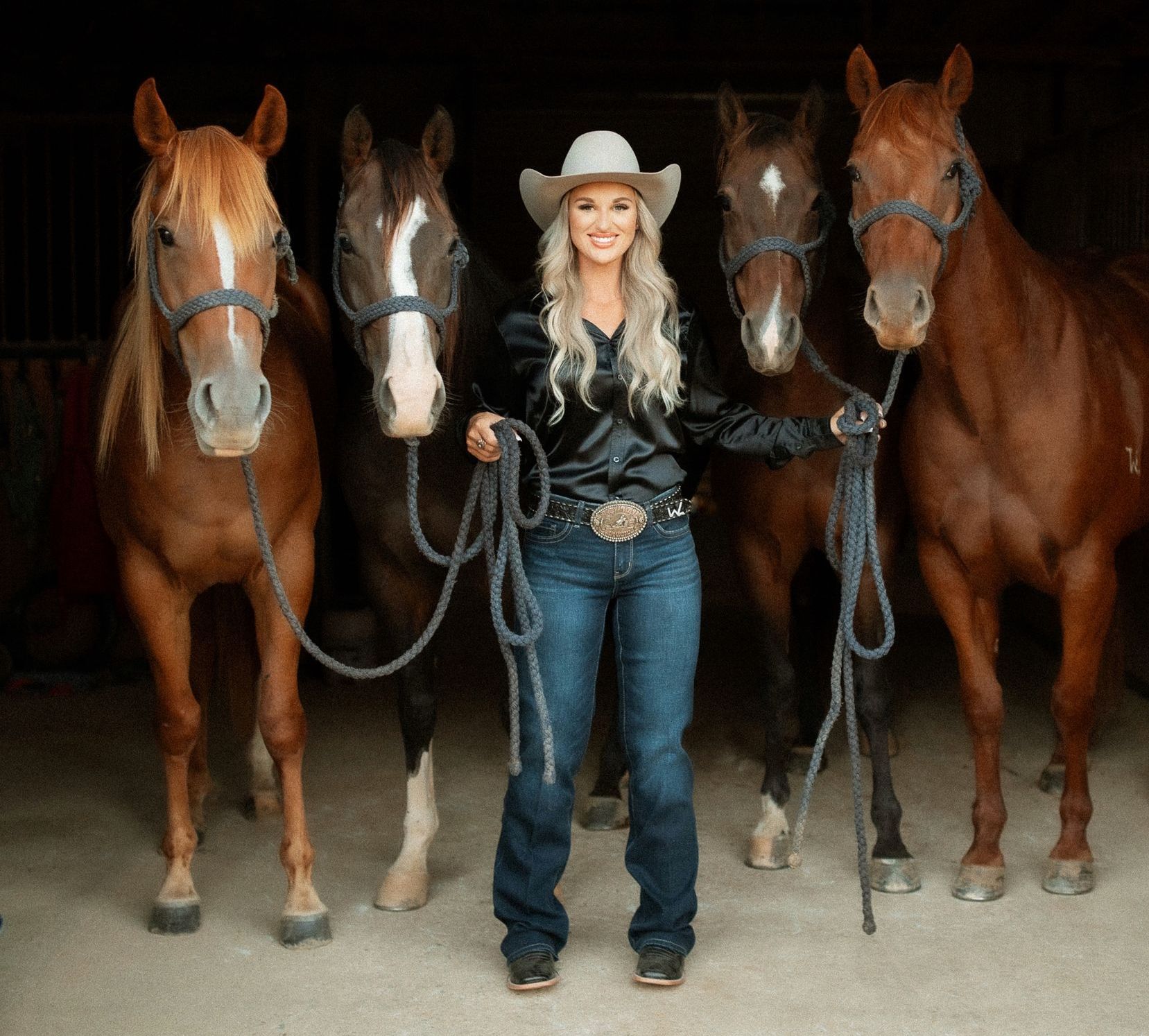 A woman in a cowboy hat stands between two brown horses