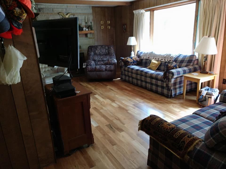 Living room with plaid couches, wooden paneling, a recliner, and a window.