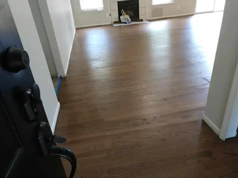 Brown hardwood floors in a sunlit living room, viewed from a dark door opening.