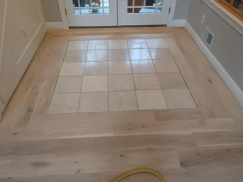 Light wood floor with a square of beige tile in front of white double doors.