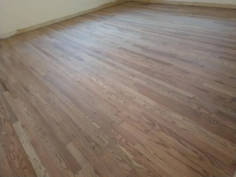 Newly stained hardwood floor in a room, angled view. Brown tones with some lighter areas and a beige wall.