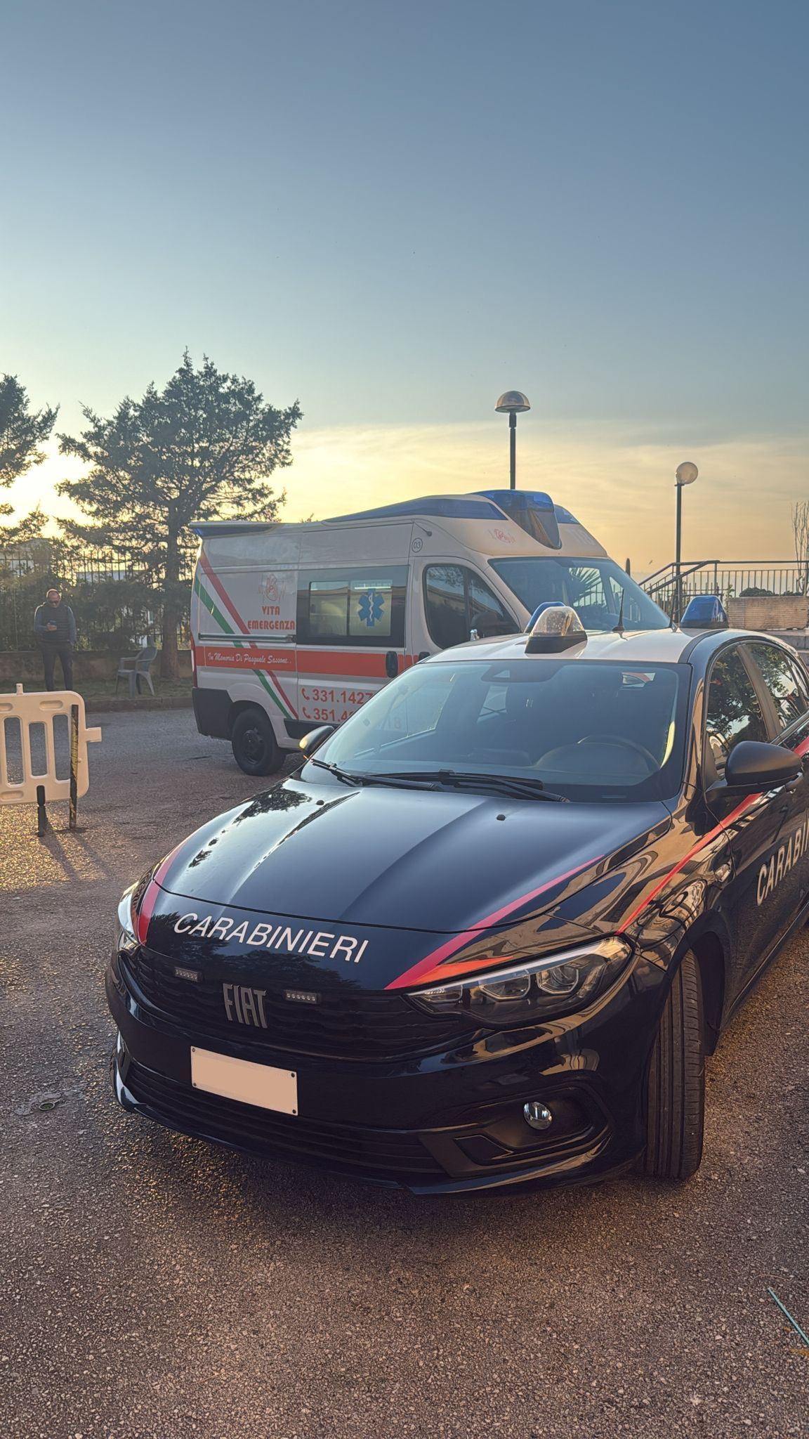 Un'auto Honda nera parcheggiata all'aperto al tramonto, con un furgone bianco e degli alberi sullo sfondo.