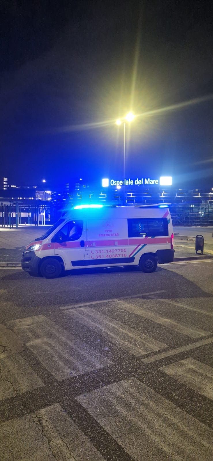 Furgone della polizia con luci blu lampeggianti parcheggiato di notte davanti a un edificio illuminato