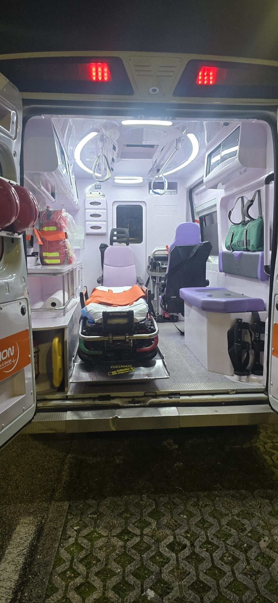 All'interno di un'ambulanza, con barella e attrezzature mediche visibili all'ingresso posteriore.
