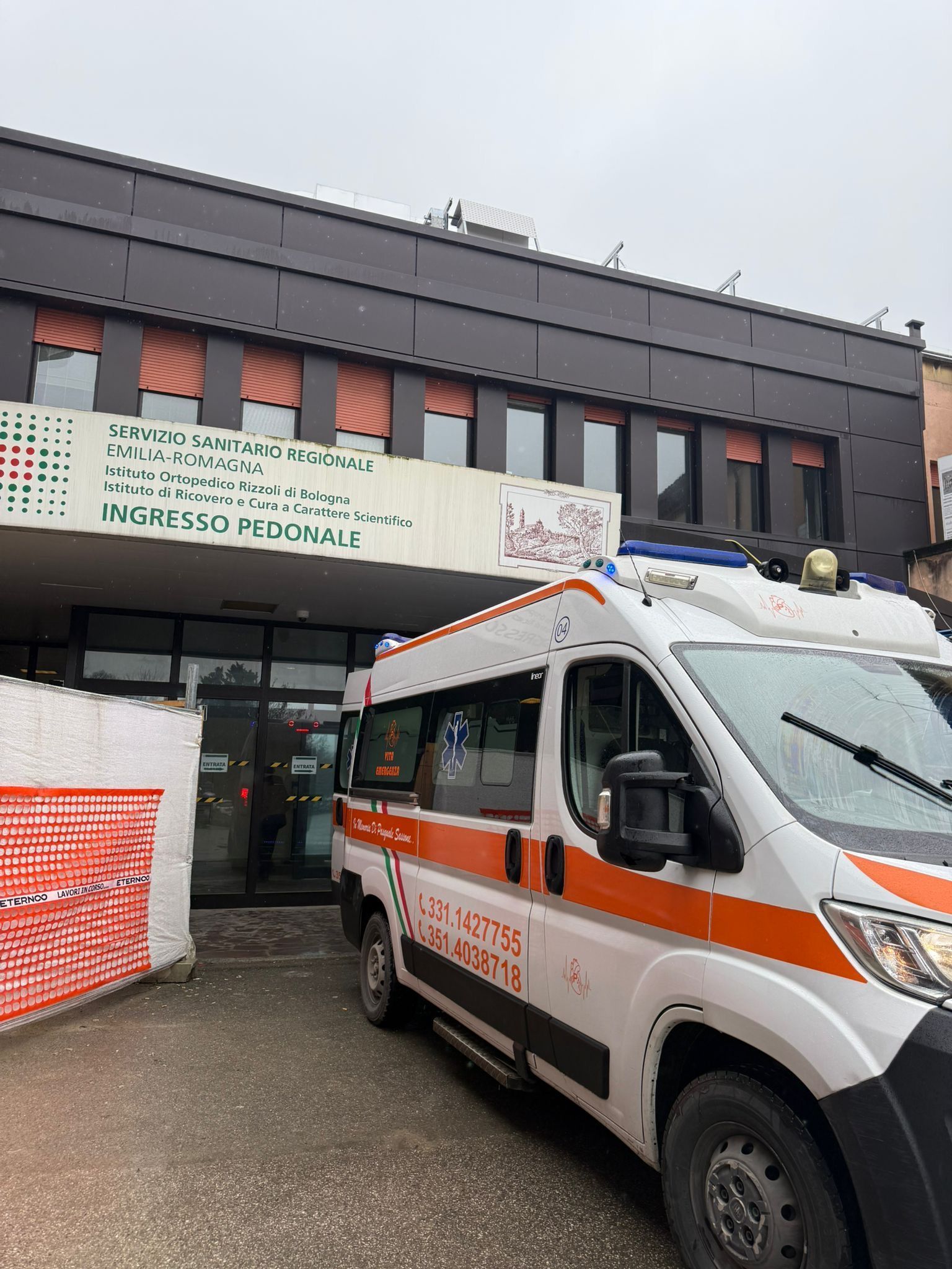 Un'ambulanza è parcheggiata davanti a un edificio con l'insegna del Vicks Vaporub e barriere da cantiere rosse e bianche.