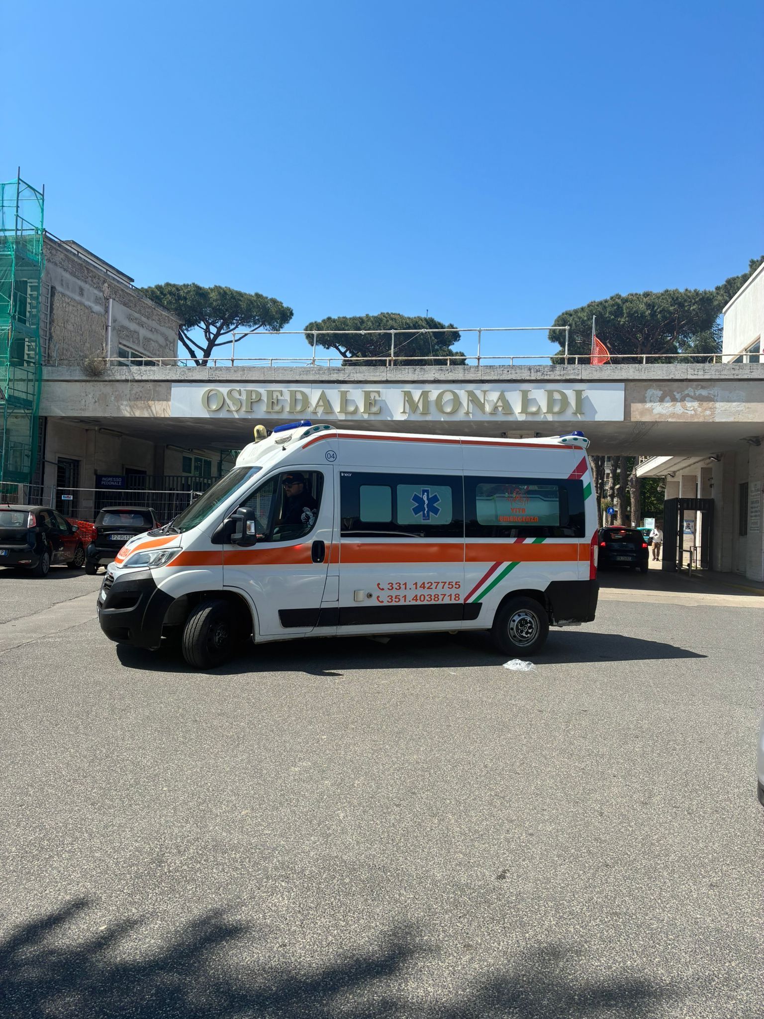 Un'ambulanza parcheggiata davanti all'ingresso di un ospedale, sotto un cielo azzurro e limpido.
