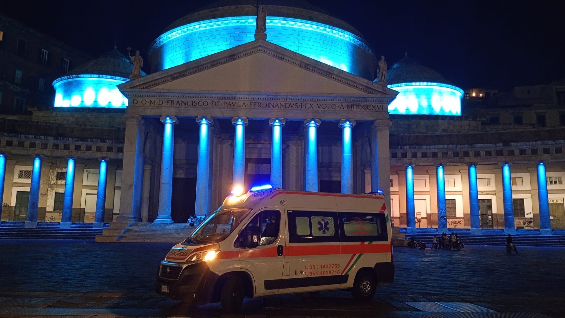 Un'ambulanza parcheggiata di notte davanti a un edificio neoclassico illuminato di blu.