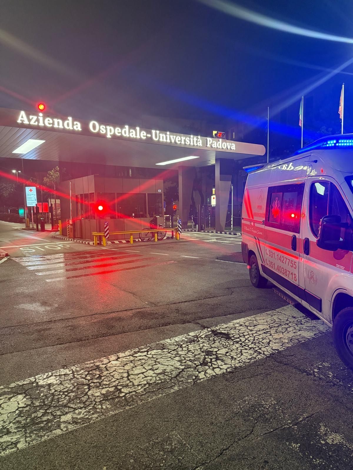 Nighttime at Azienda Ospedale-Università entrance with a police van and barricades on a wet street.