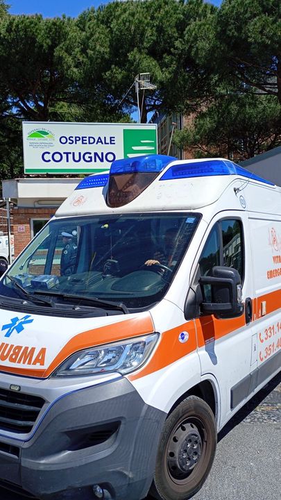 Ambulanza parcheggiata fuori dall'ospedale di Cotugno con un cartello verde e alberi sullo sfondo.