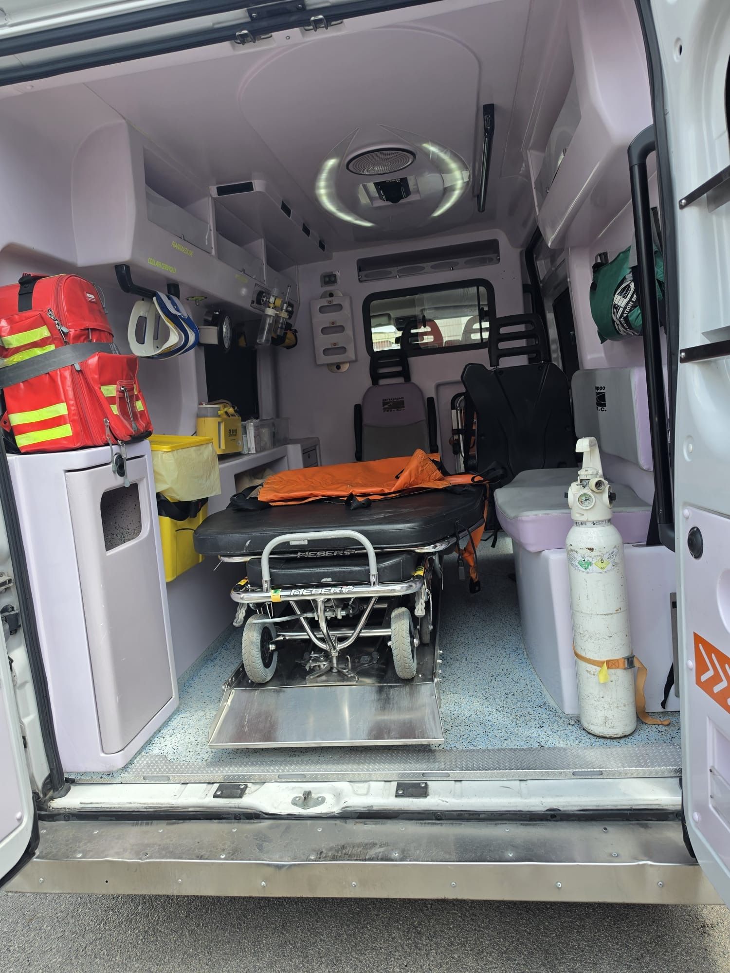 Interno dell'ambulanza con barella, attrezzatura medica e bombole di ossigeno pronte per il trasporto.