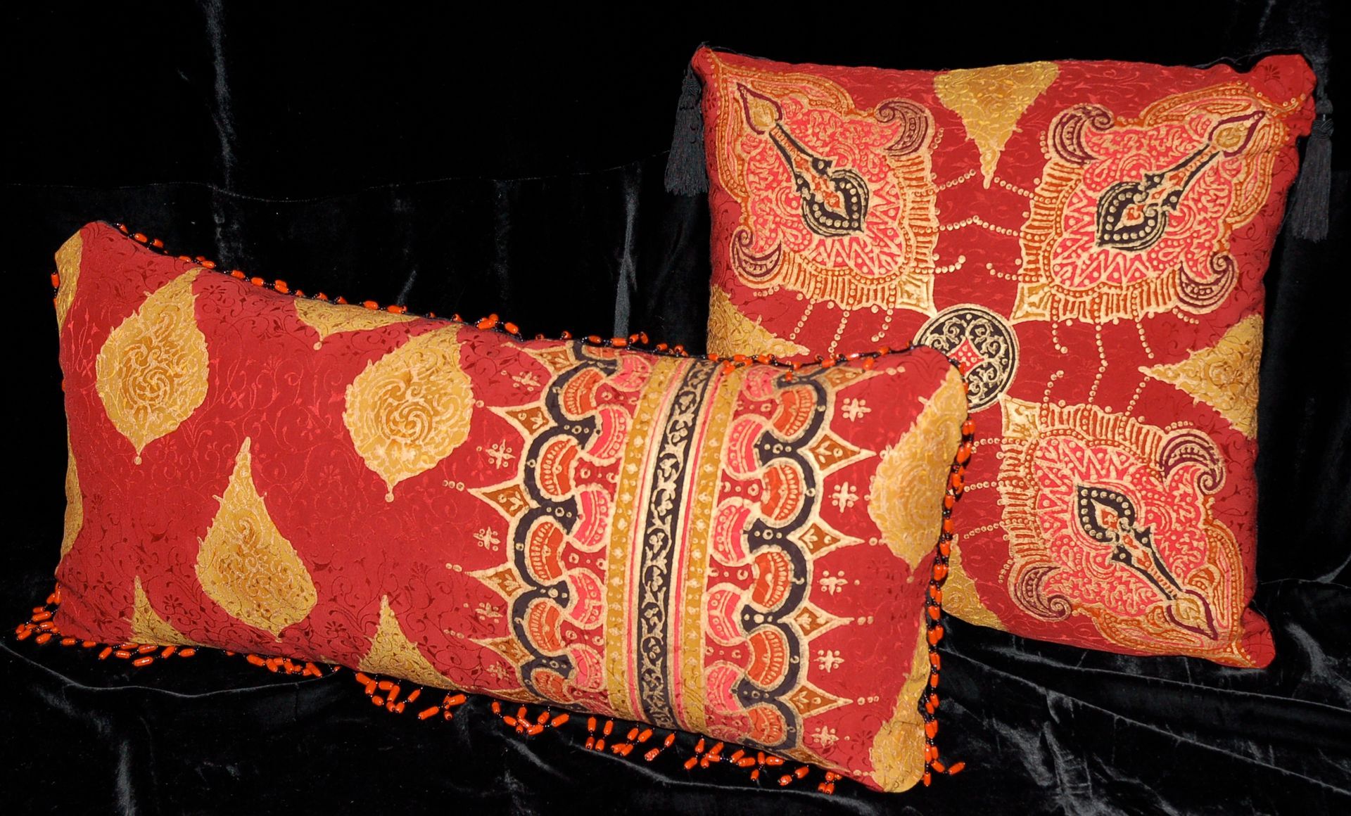 Two decorative red and gold patterned pillows against a black background.