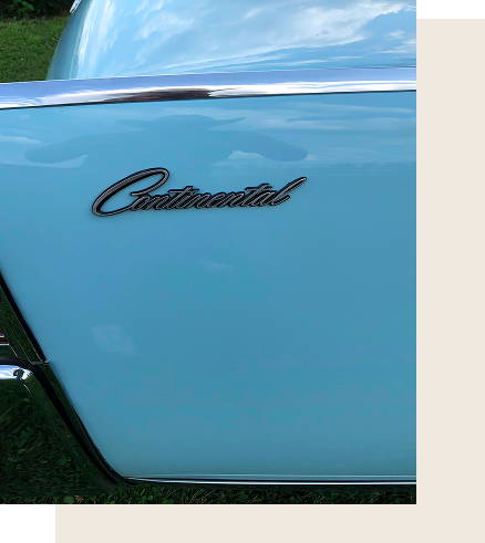 Light blue Lincoln car with a person wearing a cowboy hat in the driver's seat; people in the background.