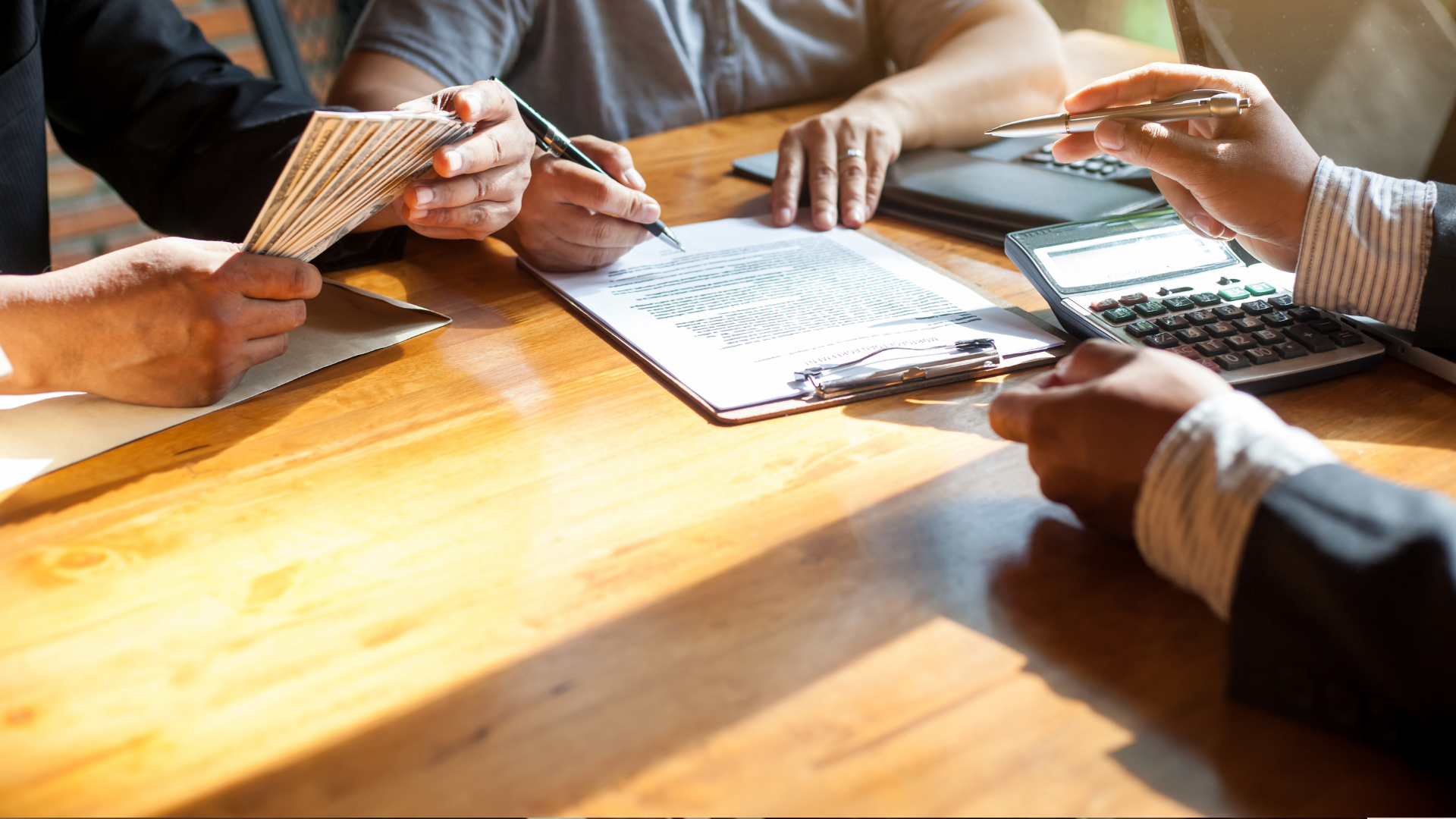 Hands of several people meeting around a wooden table with papers, a laptop, and a calculator.