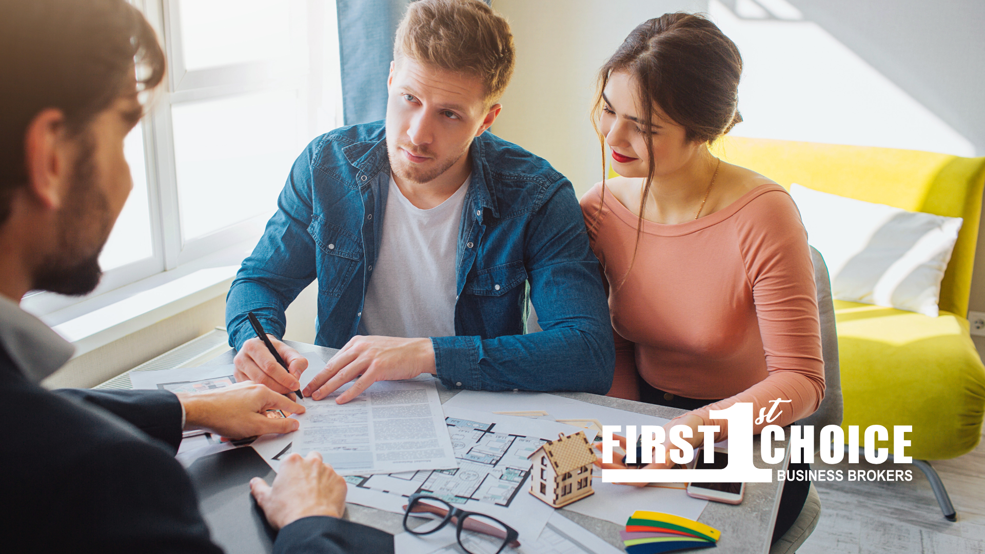 A man and a woman are sitting at a table looking at a blueprint of a house.