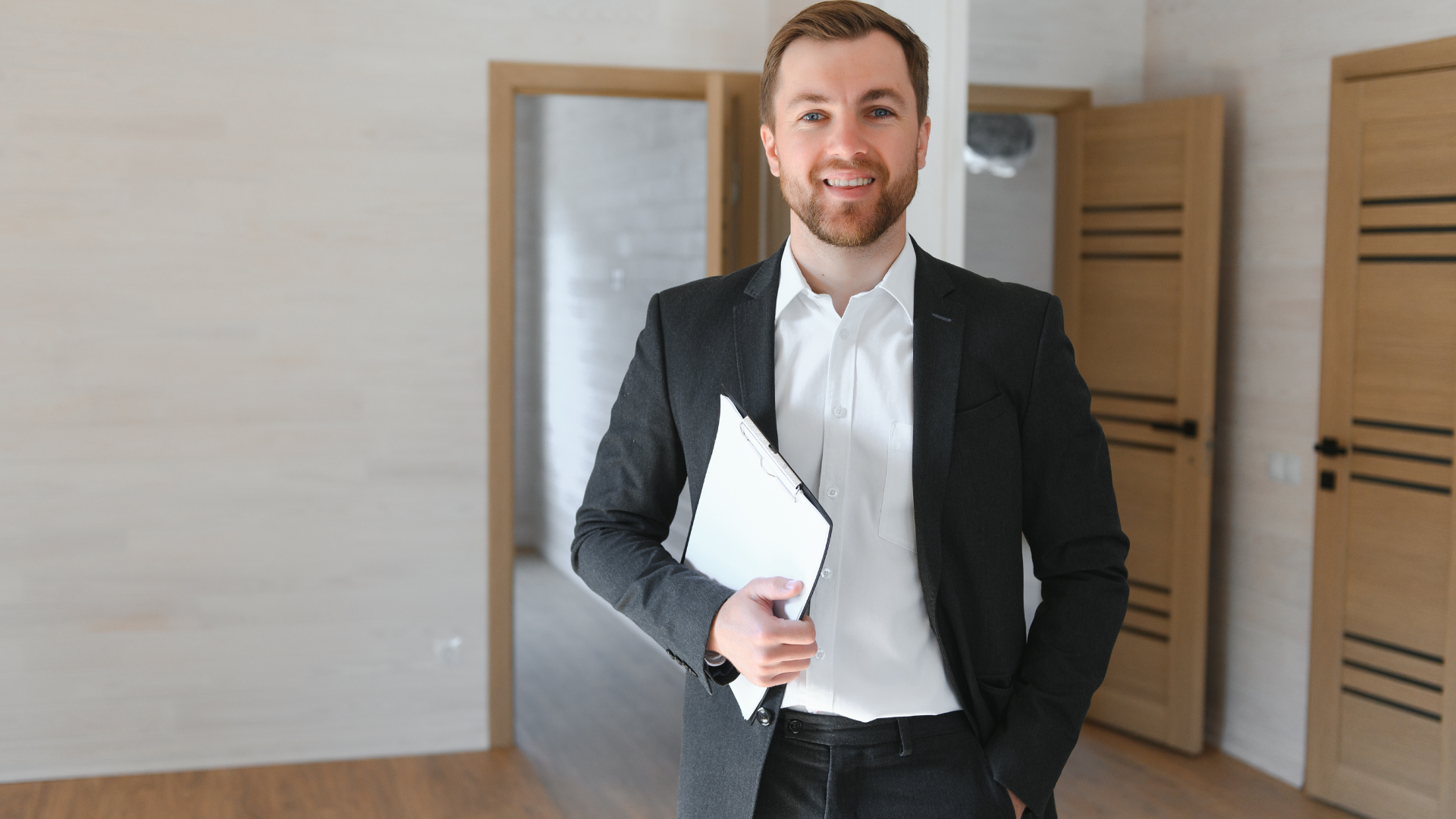 Real estate agent smiling, holding clipboard, standing in empty room with open doors.