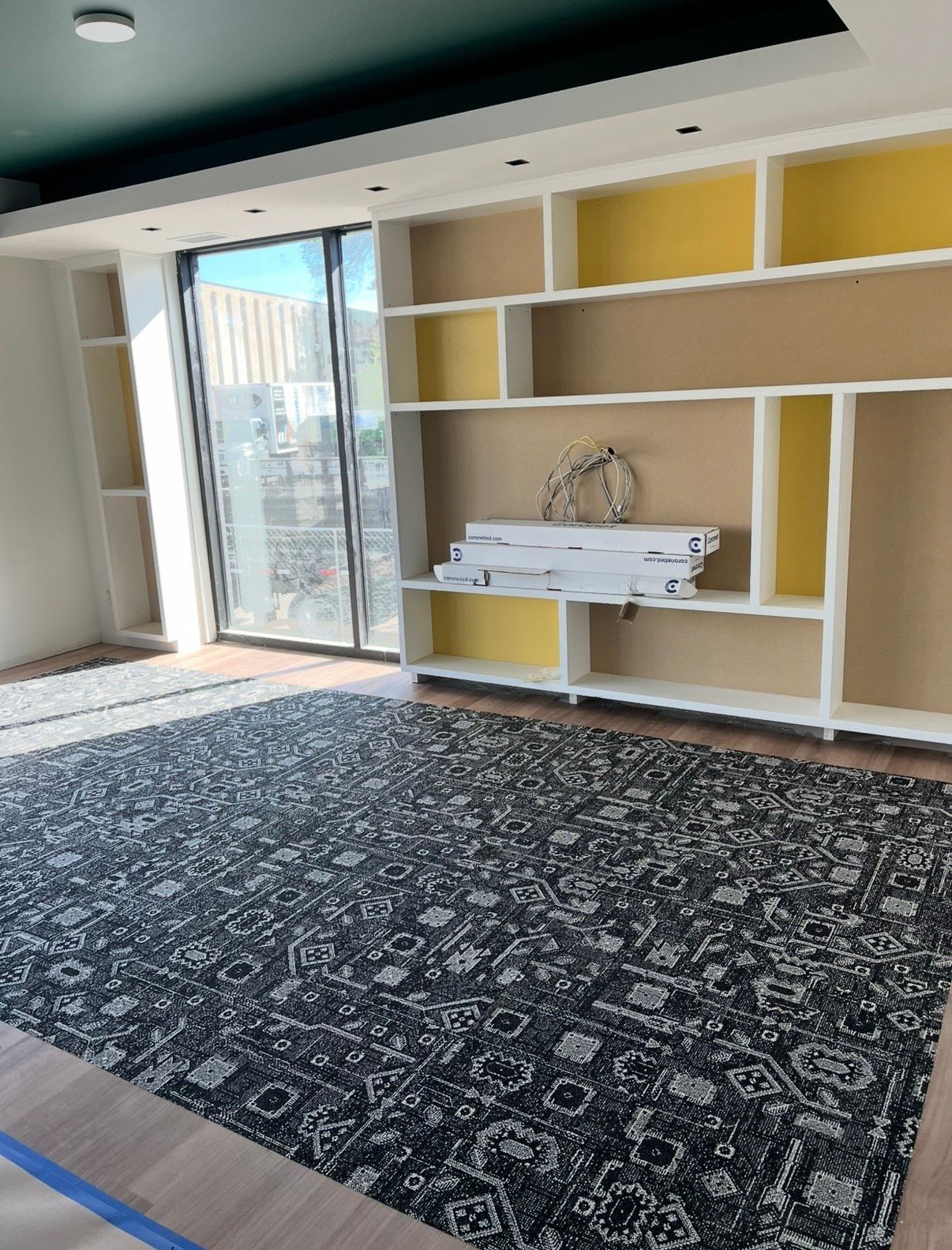 Room with a dark rug, built-in white shelves with yellow backs, and a sliding glass door.