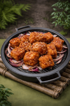 Glazed fried chicken pieces on a black grill pan over onion slices, set on bamboo in a rustic outdoor scene