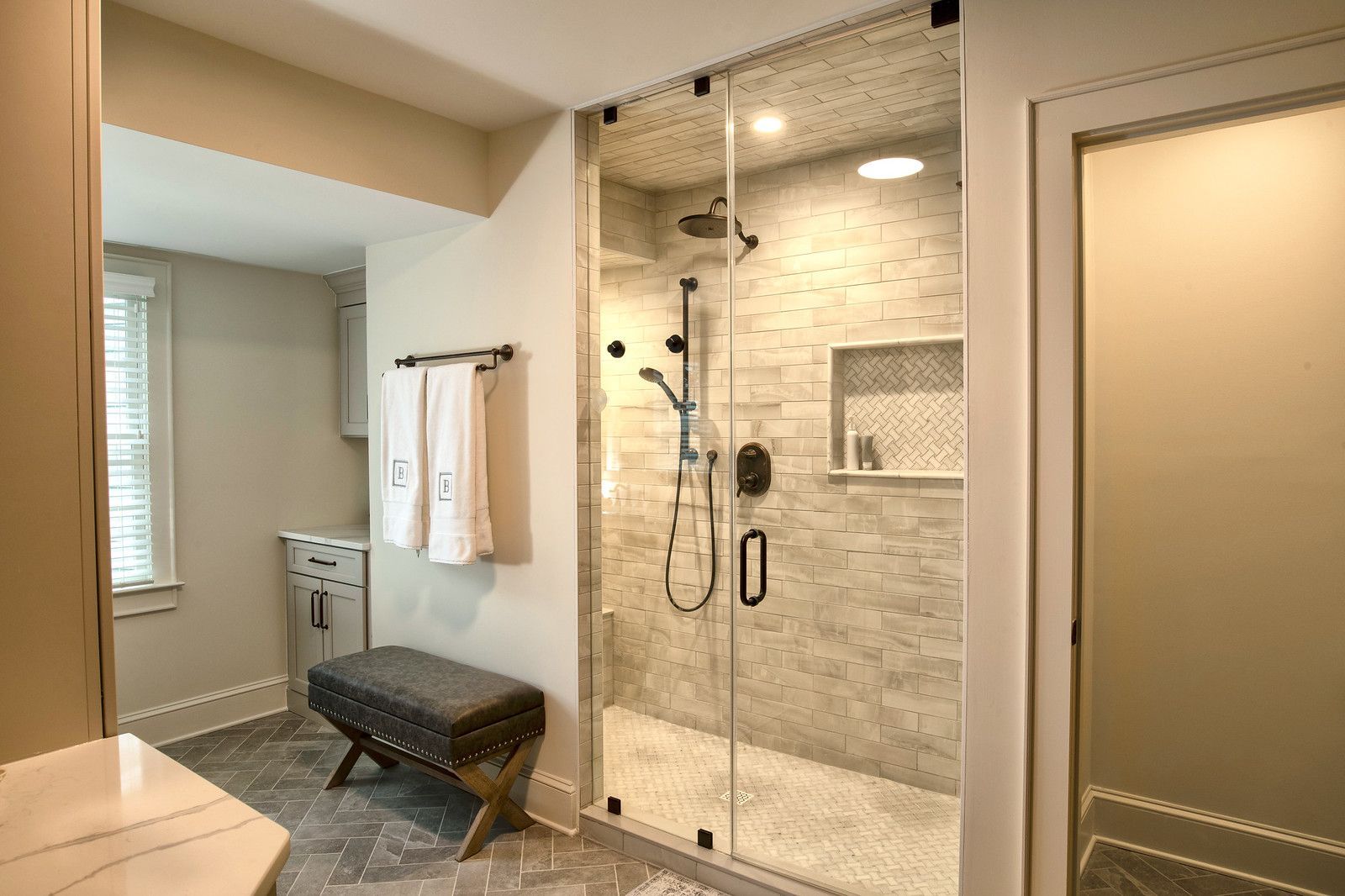 Accessible bathroom with glass shower, bench, grab bars, and beige tile.