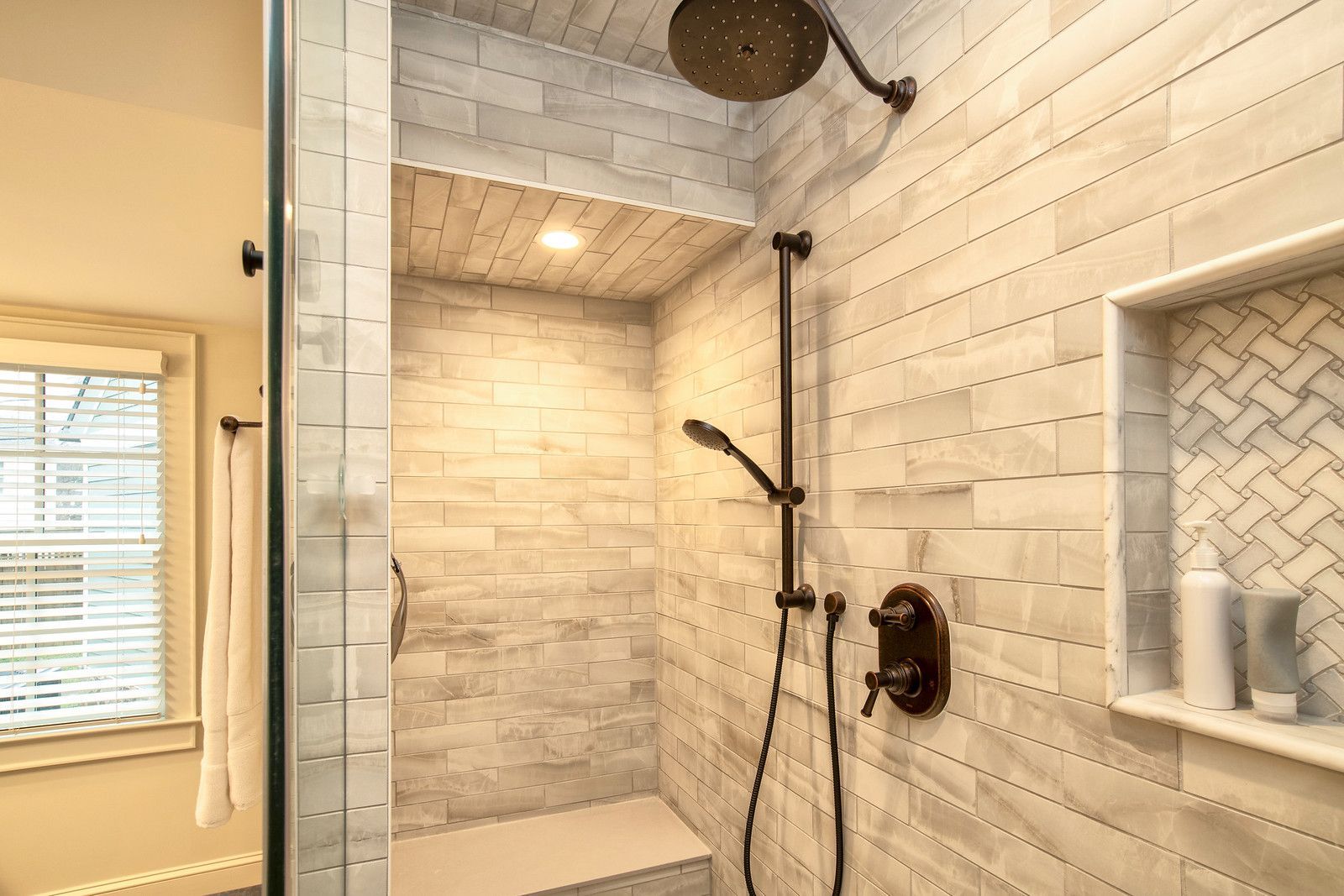 Modern white-tiled walk-in shower with rain showerhead and built-in shelf