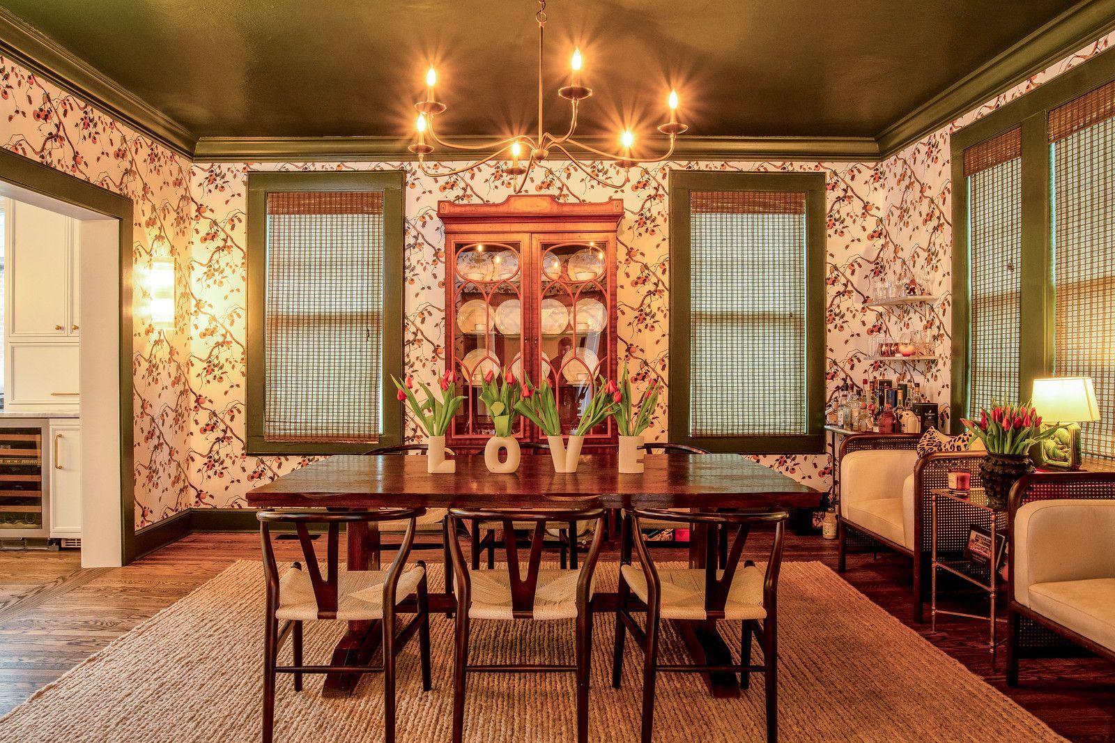 Vintage dining room with floral wallpaper, wooden table, chairs, and green-framed windows