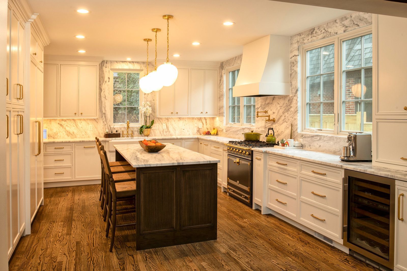 Bright modern kitchen with white cabinets, marble island, pendant lights, and wood flooring