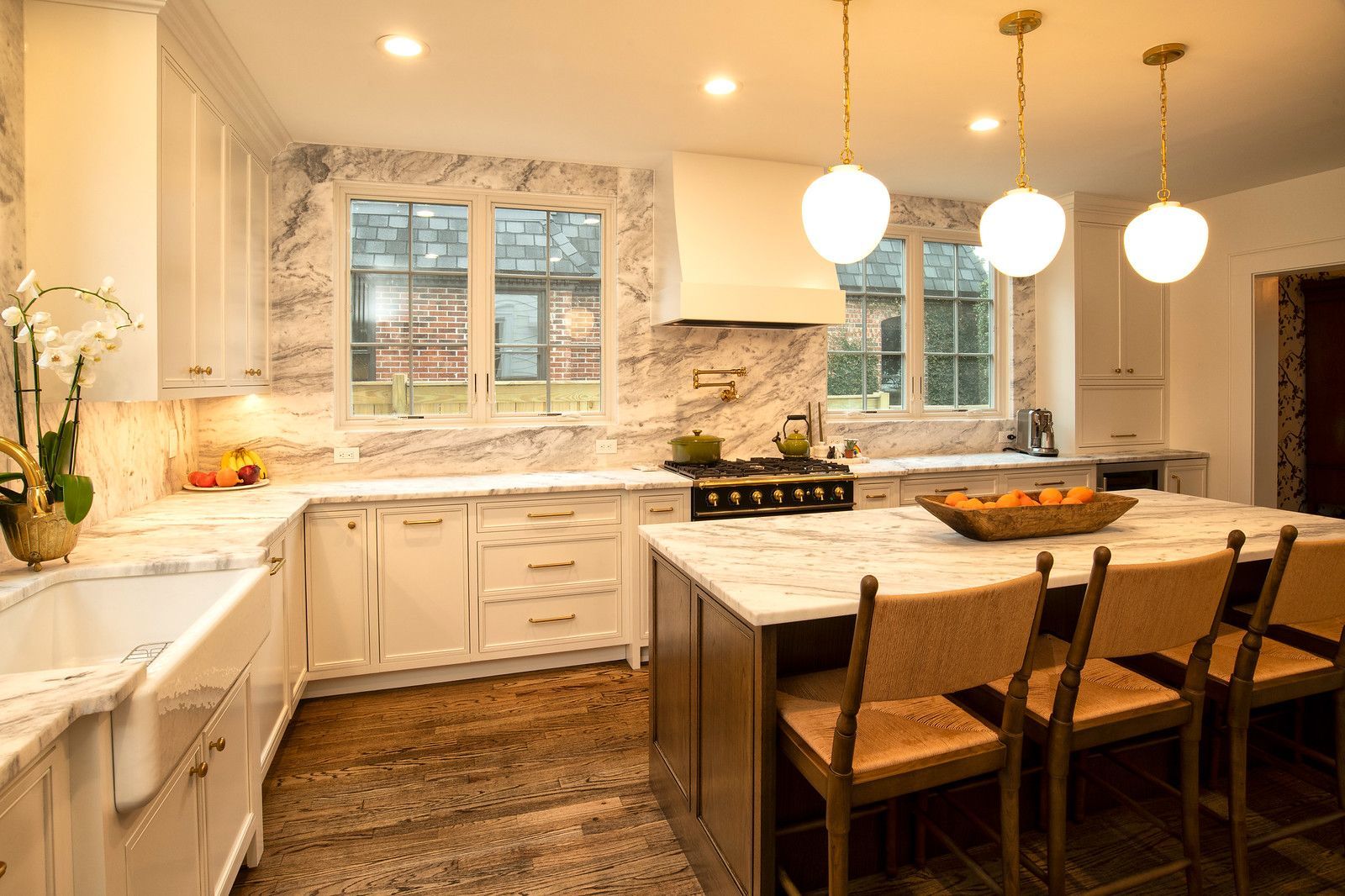 Bright modern kitchen with white cabinets, wood island, and three pendant lights under large windows