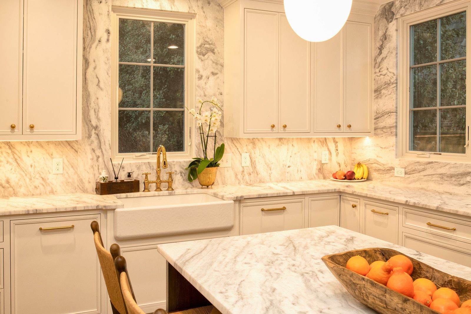 Bright white kitchen with marble counters, farmhouse sink, and a bowl of oranges on the island.