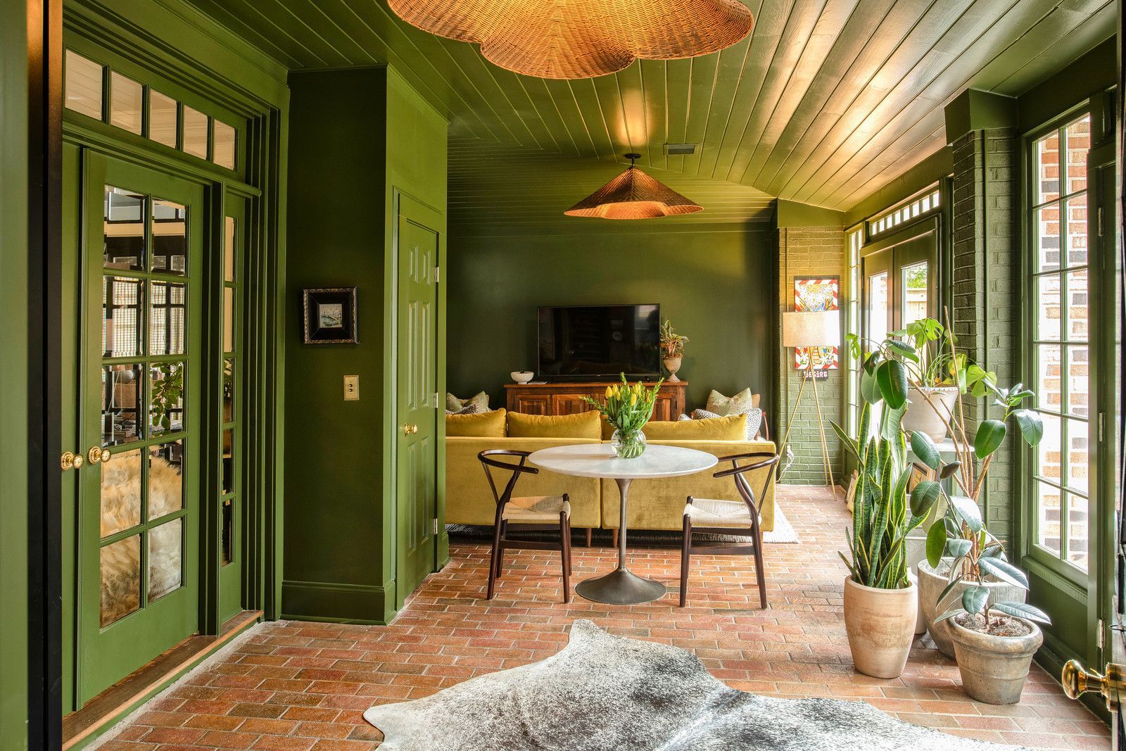 Green sunroom with large windows, a table, potted plants, and a rug on a tiled floor.
