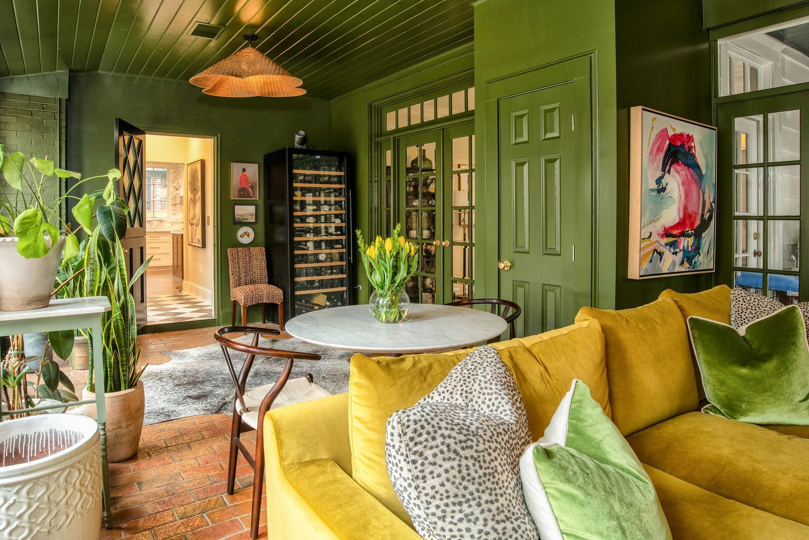 Green living room with yellow sofa, plants, patterned chairs, and open doors to a bright hall