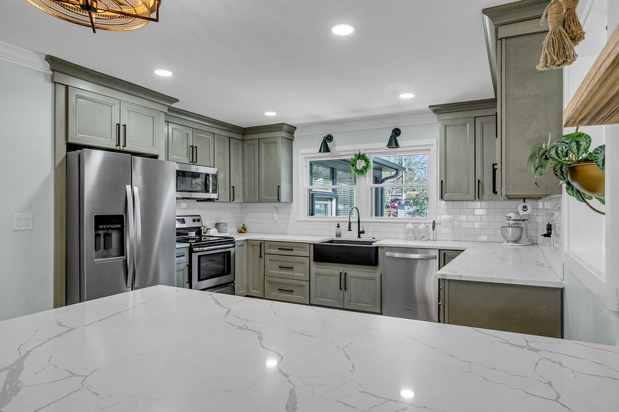Bright modern kitchen with white marble island, gray cabinets, stainless appliances, and a window over the sink