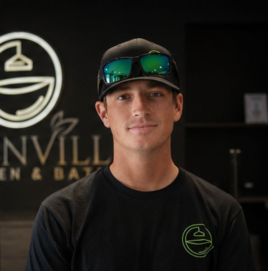 Smiling person in a black cap and shirt standing in front of a business sign