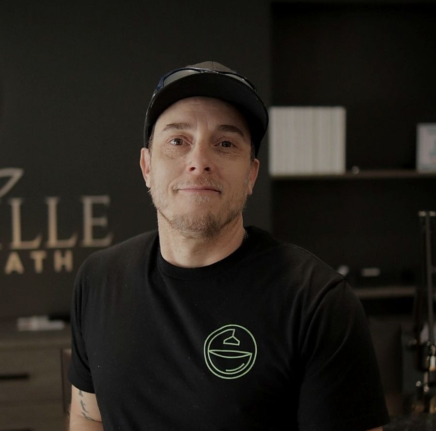 Person in a black cap and T-shirt standing in a modern cafe, with shelves and a logo in the background
