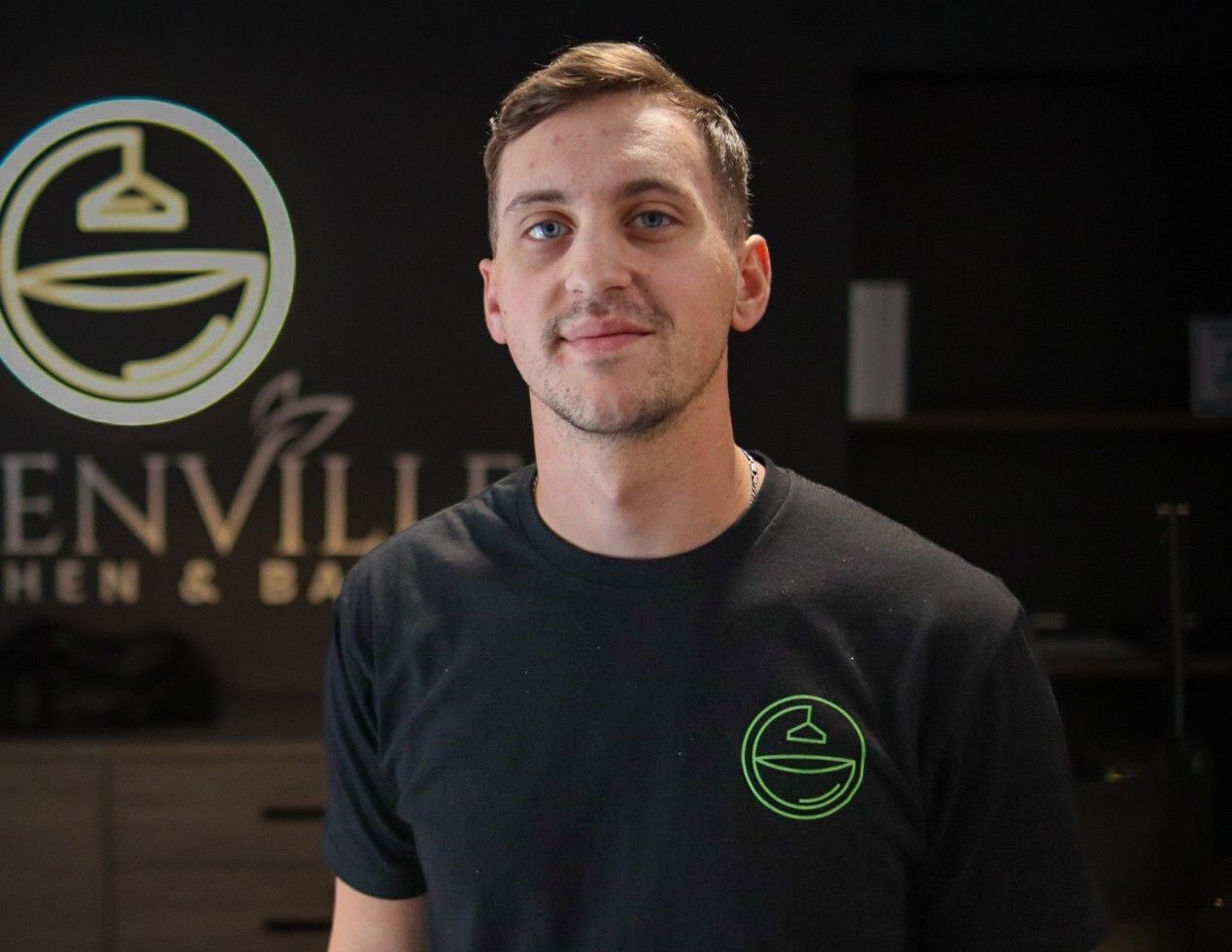 Man standing in a black T-shirt with a green logo inside a dark business office