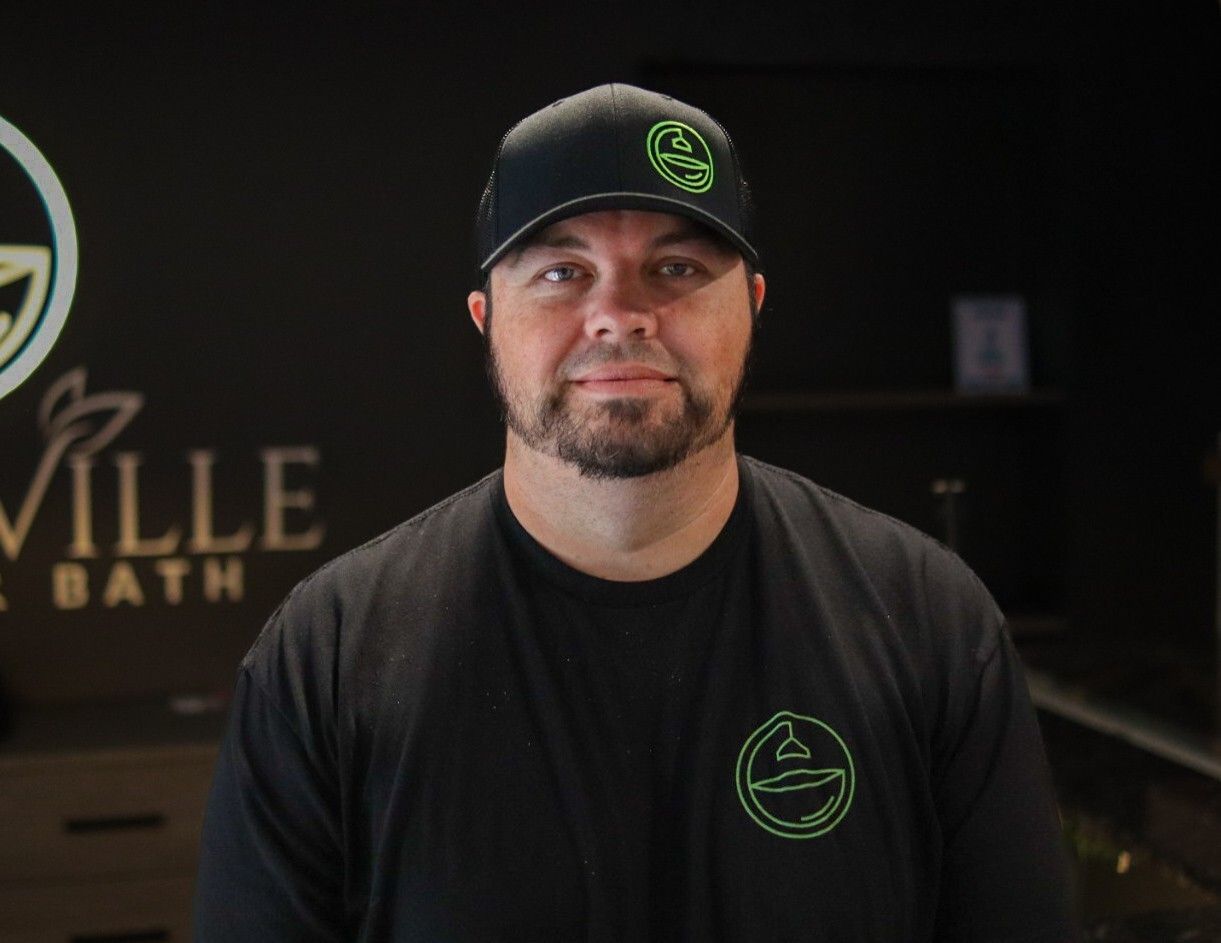 Man in black cap and shirt with green logo standing indoors against a dark background