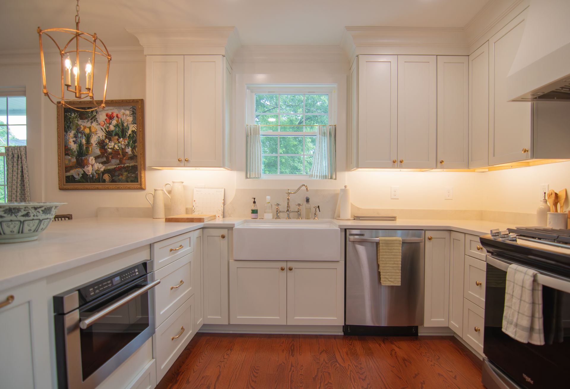 Bright white kitchen with stainless steel appliances, window over sink, and wood floor.
