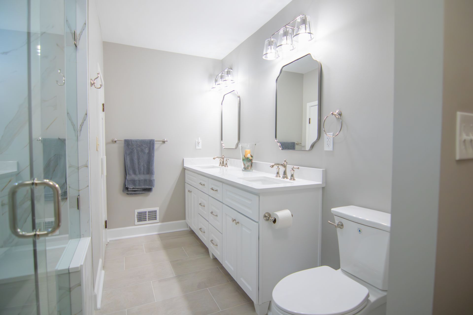 Bright modern bathroom with double vanity, mirror, toilet, and glass shower stall