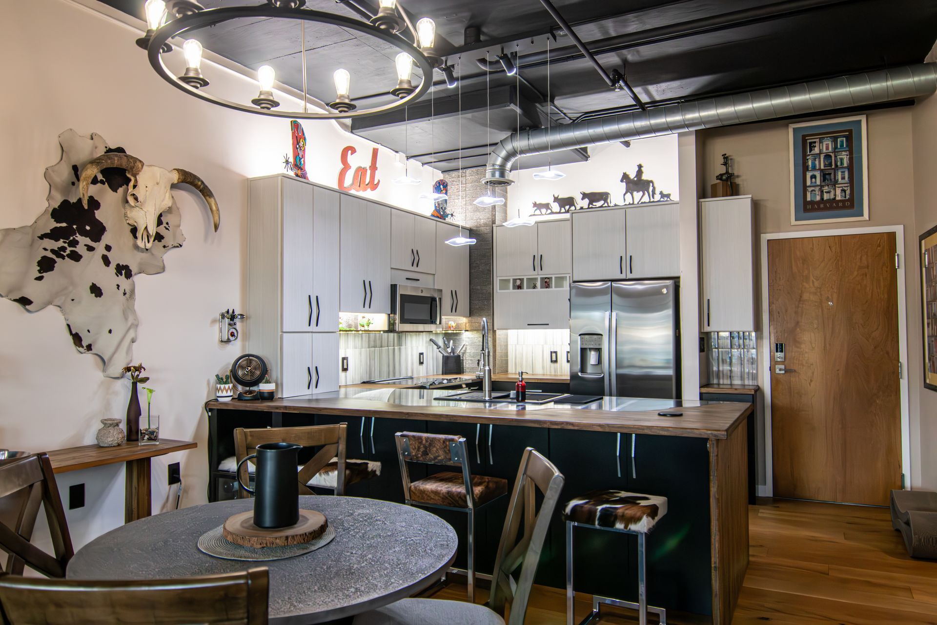 Modern kitchen with island, stainless appliances, bar stools, and a round table under a hanging light