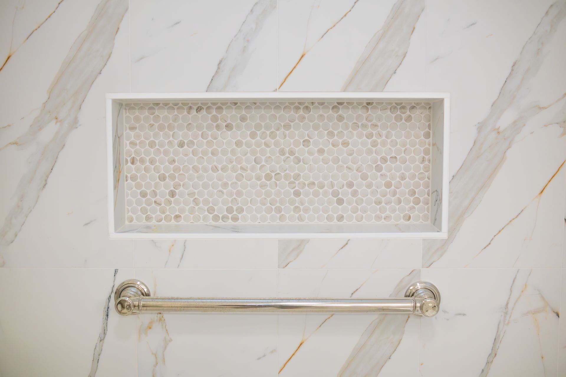 Gold towel bar beneath a rectangular recessed wall niche on a white marble-patterned bathroom wall