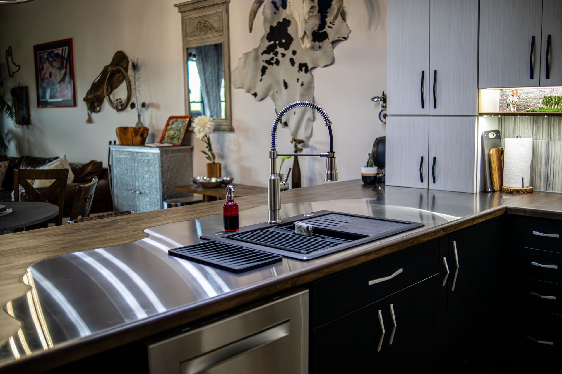 Modern kitchen with black countertops, sink, and cabinets overlooking a living room area